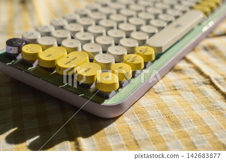 Retro-style beige and yellow keyboard on checkered fabric with sunlight shadows Retro-style beige and yellow keyboard on checkered fabric with sunlight shadows 142683877