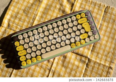 Retro style mechanical keyboard on checkered yellow fabric in sunlight Retro style mechanical keyboard on checkered yellow fabric in sunlight 142683878