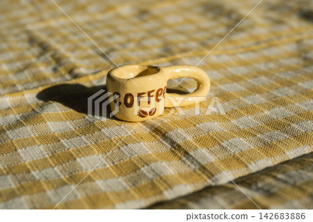 Miniature coffee cup on checkered fabric: playful details in everyday textiles Miniature coffee cup on checkered fabric: playful details in everyday textiles 142683886