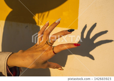 Colorful manicured hand casting shadow against yellow and white wall Colorful manicured hand casting shadow against yellow and white wall 142683923