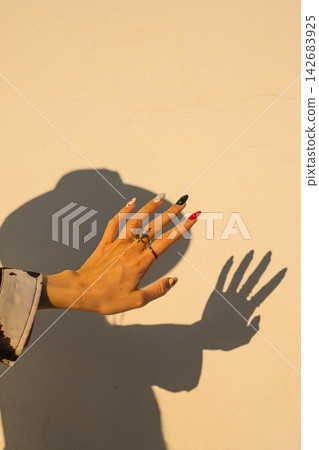Colorful manicured hand casting shadow on sunlit wall for fashion concepts Colorful manicured hand casting shadow on sunlit wall for fashion concepts 142683925