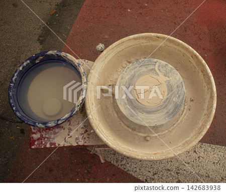 Manual pottery wheel with wet clay and basin of water on red surface Manual pottery wheel with wet clay and basin of water on red surface 142683938
