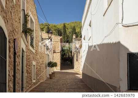 Paved street leading uphill in a village with stone and whitewashed buildings under a clear blue sky 142683970