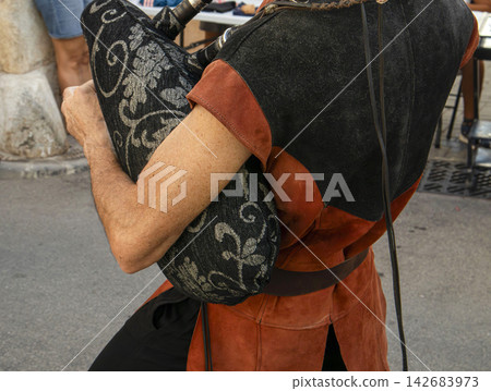 Musician carrying a black and silver patterned bagpipe over their shoulder in a street setting Musician carrying a black and silver patterned bagpipe over their shoulder in a street setting 142683973