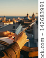 Person journaling on rooftop with cityscape view at sunset 142683991