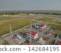 Industrial energy facility processes materials through interconnected buildings, storage tanks, towers, and elevated pipelines. Paved service roads and surrounding forest emphasize large scale 142684195