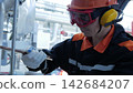 Factory worker grips steel pipe inside modern processing plant, focused young adult man in protective gear performing maintenance near polished machinery and bright stainless steel structures. 142684207
