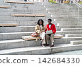 Fashionable African American student friends talking beside laptop on wide urban steps downtown 142684330