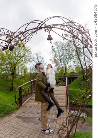 Smiling young man lifts his girlfriend beneath an ornate iron arch Smiling young man lifts his girlfriend beneath an ornate iron arch 142684579