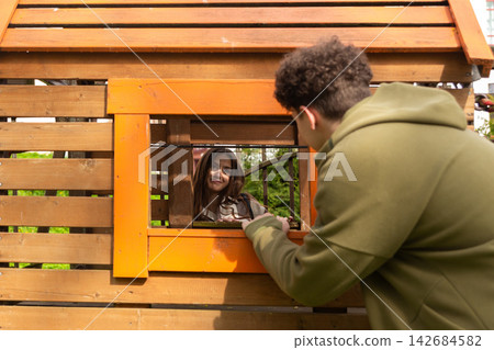 Young couple playfully interact through a wooden playground structure Young couple playfully interact through a wooden playground structure 142684582