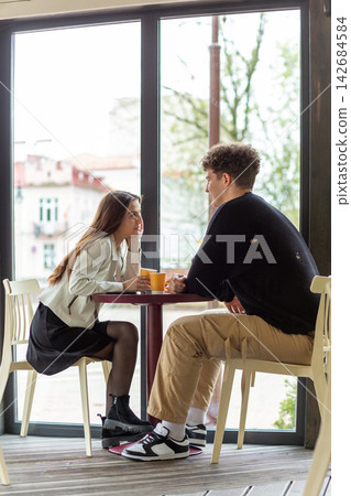 Young couple enjoying coffee together at a cafe table by large window Young couple enjoying coffee together at a cafe table by large window 142684584