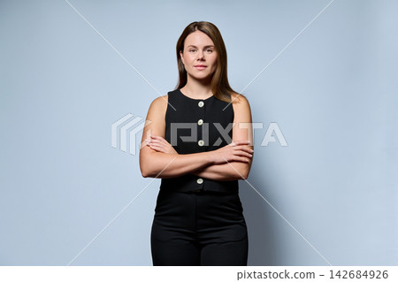 Confident businesswoman standing with arms crossed on light blue background Confident businesswoman standing with arms crossed on light blue background 142684926