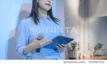 一位女講師手持平板電腦和麥克風,並在投影機上顯示代碼。 一位女講師手持平板電腦和麥克風,並在投影機上顯示代碼。 142685010