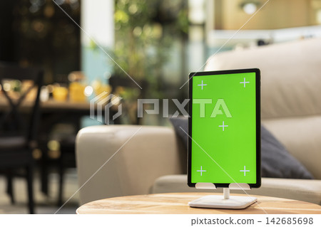 Vertical green screen on tablet in empty modern living room, device placed on a wooden coffee table. No people in apartment with cozy rustic interior design, stylish open space. 142685698