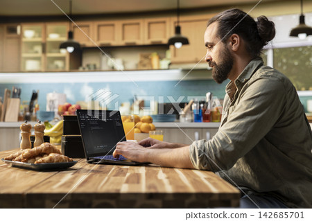Man focused on programming and software development tasks. Laptop screen displays code, scripts and binary data, illustrating system maintenance and remote work in a high-tech occupation. Man focused on programming and software development tasks. Laptop screen displays code, scripts and binary data, illustrating system maintenance and remote work in a high-tech occupation. 142685701