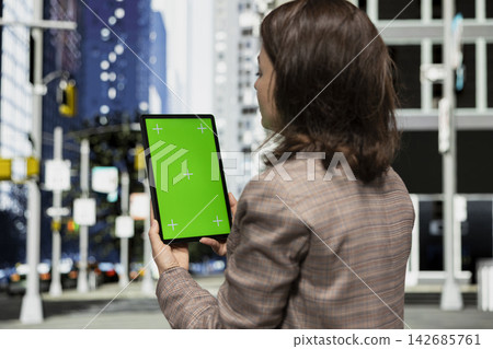 Green screen mockup tablet, walking on city sidewalk and woman reading digital book. Strolling on metropolitan avenue, chroma key isolated screen ebook reader and person doing morning commute 142685761