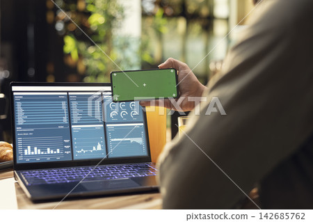 Isolated mockup on mobile phone screen used at home in kitchen, remote worker analyzing metrics and charts on laptop. Teleworking and outsourcing showing task management and research. 142685762