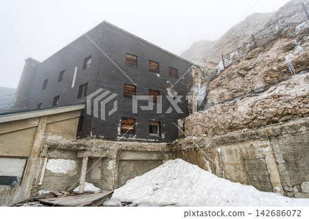 Foggy Mountain Lodge Exterior with Snow and Rocky Alpine Cliff Foggy Mountain Lodge Exterior with Snow and Rocky Alpine Cliff 142686072