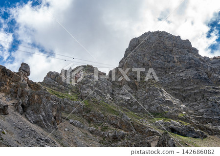 Rocky Mountain Cliff with Cable Cars and Dramatic Cloudy Sky 142686082