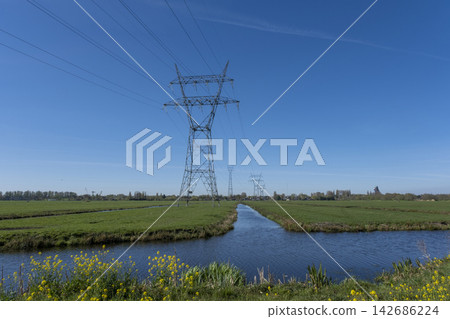 Power Lines Over Rural Canal and Green Fields Under Blue Sky Power Lines Over Rural Canal and Green Fields Under Blue Sky 142686224