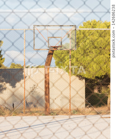 Rusty Basketball Hoop on Empty Outdoor Court Behind Fence Rusty Basketball Hoop on Empty Outdoor Court Behind Fence 142686238