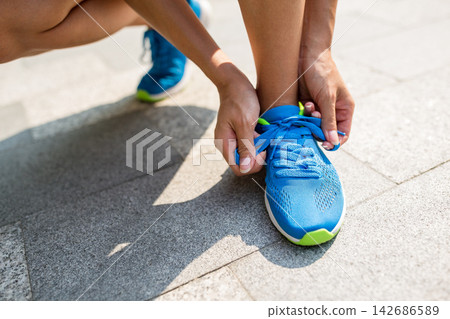 Runner Tying Blue Running Shoes on Sunny Pavement Runner Tying Blue Running Shoes on Sunny Pavement 142686589