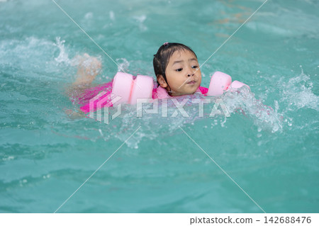 preschool child girl playing and swimming with floaties in pool water preschool child girl playing and swimming with floaties in pool water 142688476