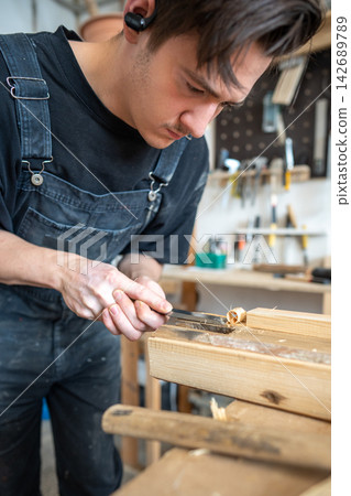 Skillful woodworker carving old layers from wooden board with chisel tool in restoration workshop. 142689789