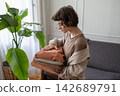 Woman examining texture of folded linen clothes while organizing wardrobe at home.  142689791