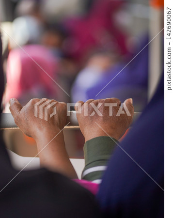 Close-up of a passenger's hand holding a handrail handle inside a public transport bus or train for balance during a daily city commute. 142690067