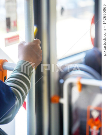 Close-up of a passenger's hand holding a handrail handle inside a public transport bus or train for balance during a daily city commute. 142690069