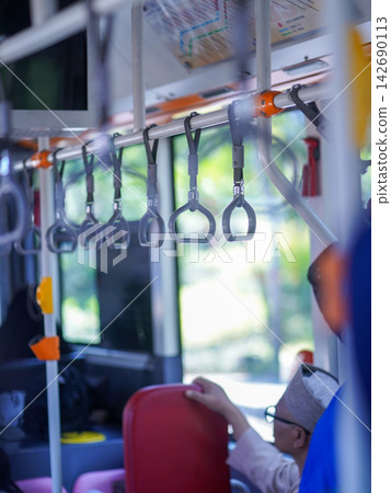 Row of hanging overhead handrail handles and grab straps inside a public transportation bus or train for passenger balance and safety. Row of hanging overhead handrail handles and grab straps inside a public transportation bus or train for passenger balance and safety. 142690113