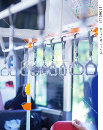 Row of hanging overhead handrail handles and grab straps inside a public transportation bus or train for passenger balance and safety. 142690114