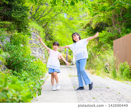姊妹倆沿著綠樹成蔭的小路愉快地散步。 姊妹倆沿著綠樹成蔭的小路愉快地散步。 142690449
