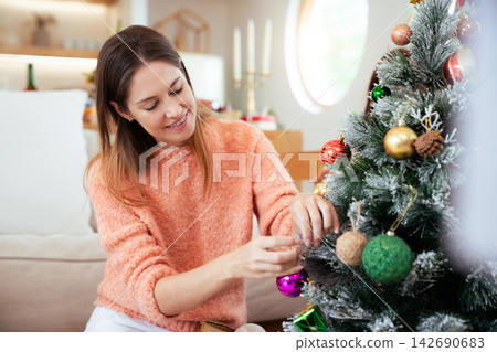 Caucasian woman decorating Christmas tree with ornaments at home 142690683