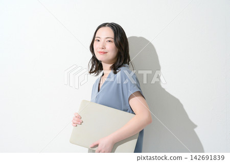 一位日本女性面帶微笑，手持筆記型電腦，背景為白色。 142691839
