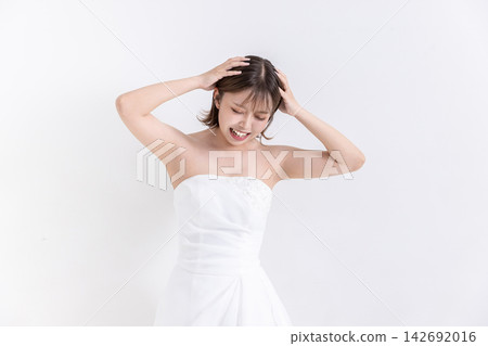 一個穿著白色洋裝的女孩站在白色背景前，雙手抱頭。 142692016