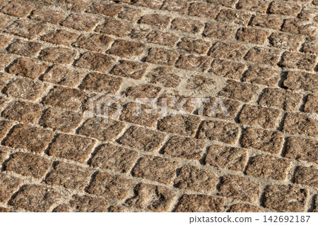 Close-up view of weathered cobblestone pavement showing square stones, sandy joints 142692187