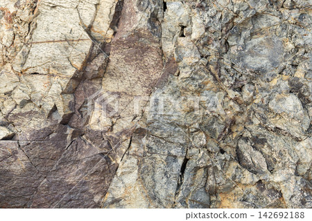 Close-up view of a layered rocky cliff wall featuring varied stone textures Close-up view of a layered rocky cliff wall featuring varied stone textures 142692188