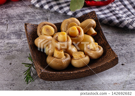 Marinated champignon mushrooms in dark wooden bowl with rosemary sprig and checkered cloth background Marinated champignon mushrooms in dark wooden bowl with rosemary sprig and checkered cloth background 142692682