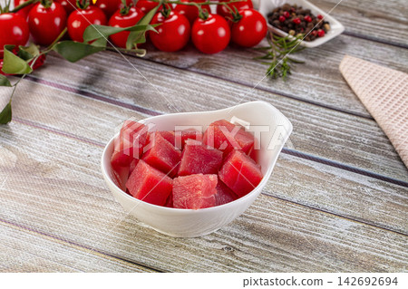 Cubed raw tuna in white ceramic bowl on weathered wooden table with cherry tomatoes and peppercorns in background Cubed raw tuna in white ceramic bowl on weathered wooden table with cherry tomatoes and peppercorns in background 142692694