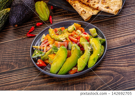Fresh avocado salad with diced tomatoes, bell peppers, and herbs served on dark plate with grilled flatbread and whole avocado on rustic wood Fresh avocado salad with diced tomatoes, bell peppers, and herbs served on dark plate with grilled flatbread and whole avocado on rustic wood 142692705