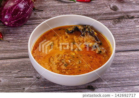 Rich orange dal curry in white bowl with roasted eggplant and red chili peppers on rustic wooden table Rich orange dal curry in white bowl with roasted eggplant and red chili peppers on rustic wooden table 142692717