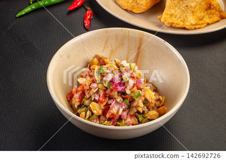 Spicy peanut sambal in ceramic bowl with red and green chilies, fried snacks in background on dark textured surface Spicy peanut sambal in ceramic bowl with red and green chilies, fried snacks in background on dark textured surface 142692726