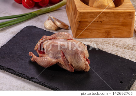 Raw whole quail on black slate with fresh garlic, green onions, and tomatoes, gourmet poultry preparation Raw whole quail on black slate with fresh garlic, green onions, and tomatoes, gourmet poultry preparation 142692765