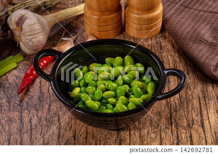 Fresh green edamame beans in black ceramic bowl on rustic wooden table with garlic, red chili and wooden salt and pepper grinders Fresh green edamame beans in black ceramic bowl on rustic wooden table with garlic, red chili and wooden salt and pepper grinders 142692781