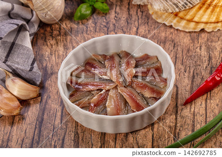 Anchovy fillets in white ceramic bowl on rustic wooden table with garlic basil red chili and green onion Anchovy fillets in white ceramic bowl on rustic wooden table with garlic basil red chili and green onion 142692785