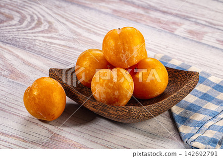 Yellow plums in rustic wooden bowl on weathered wood table with blue and white checkered cloth beside Yellow plums in rustic wooden bowl on weathered wood table with blue and white checkered cloth beside 142692791