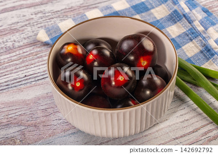 Dark cherry tomatoes in white ceramic bowl on rustic wood with blue checkered cloth and green onions beside Dark cherry tomatoes in white ceramic bowl on rustic wood with blue checkered cloth and green onions beside 142692792