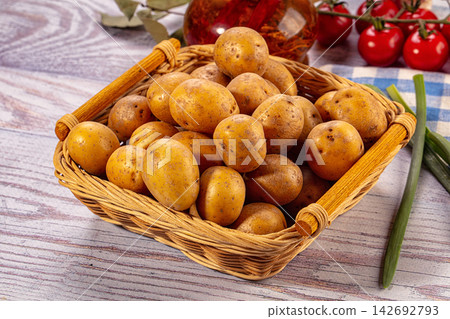 Fresh unpeeled potatoes in woven basket on rustic wooden table with cherry tomatoes and green onions nearby 142692793